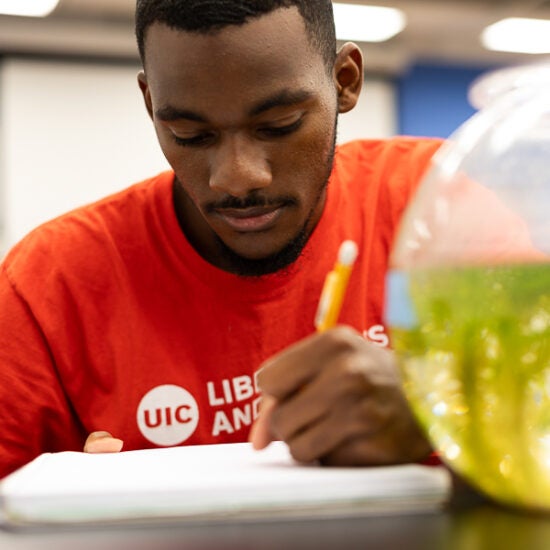 Student Emmanuel Seaton writing in notebook with red t shirt on