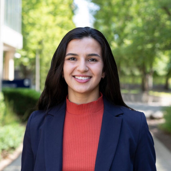 Student advisor Trisha Garcia in a red blouse and blue blazer on a college campus